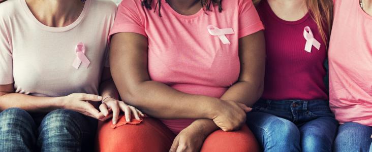 vier vrouwen zitten zij aan zij en dragen de 'pink ribbon'