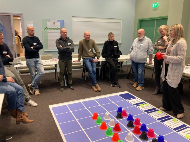 groep mensen staat voor een groot bord op de grond, met hierop pionnen