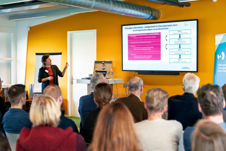 vrouw geeft presentatie voor een groep mensen in een zaal