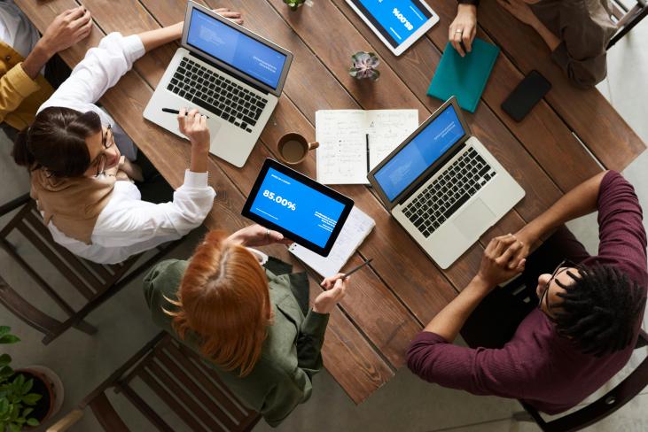 Groep mensen van bovenaf gefotografeerd, werken aan een tafel op laptops