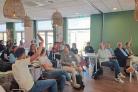 Groep mensen in een zaal, een deel steekt hun hand op.