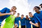 Groep tienervoetballers in blauwe shirts op een groen veld die elkaar omhelzen na het scoren van een doelpunt