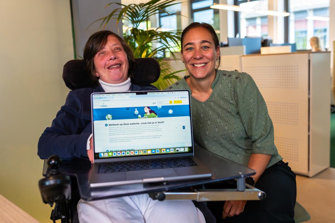 2 vrouwen, waarvan er 1 een laptop vasthoudt en presenteert