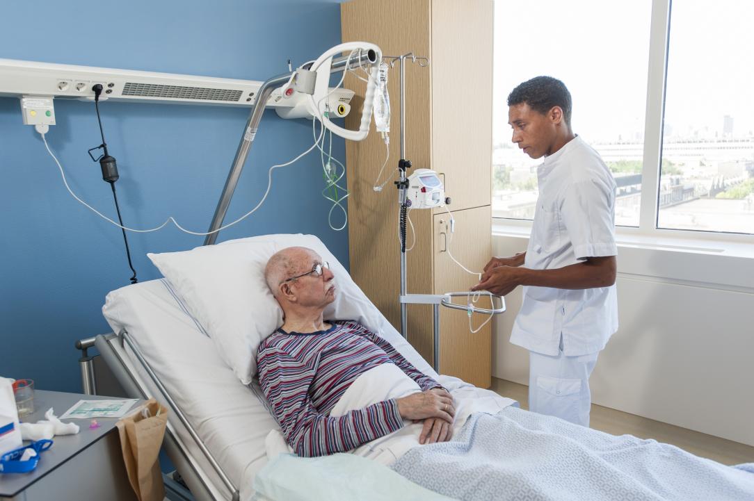Verpleegkundige brengt infuus aan bij patiënt op bed