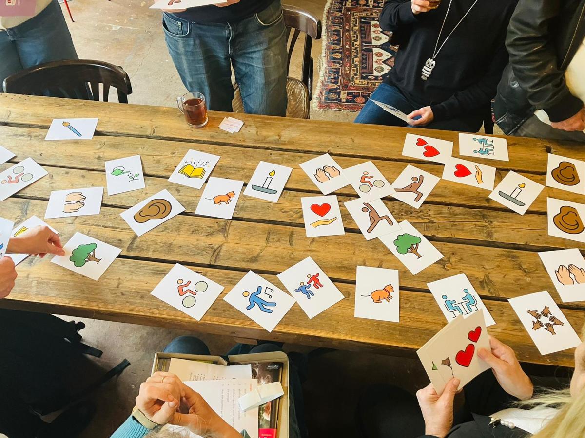 Mensen staan rond een tafel met kaarten van de kaartenset In 'Gesprek over Zingeving’