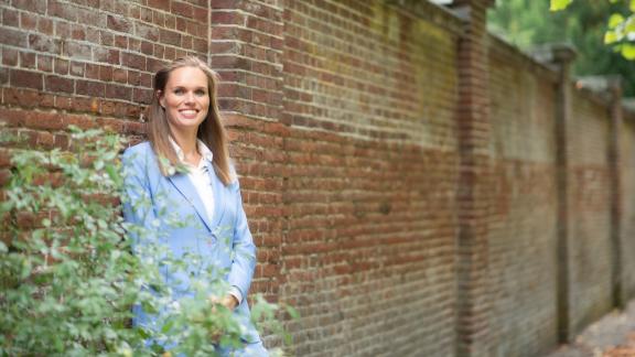 Een vrouw in een blauw pak staat tegen een muur aan geleund.