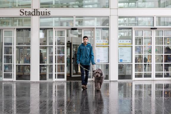 Man loopt met blindengeleidehond het stadhuis uit.