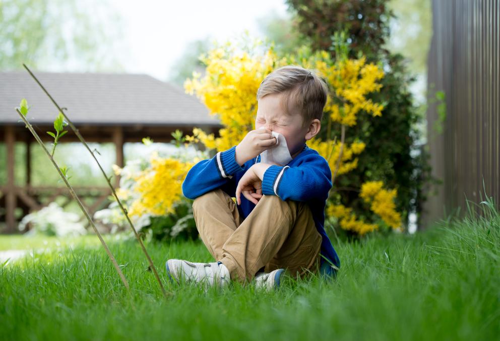 Jongetje zit in het gras met gele bloemen op de achtergrond en niest