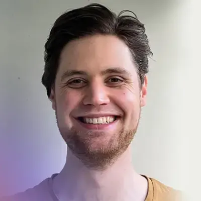 Portretfoto van een witte man met kort, bruin haar en een kort baardje. Hij lacht breeduit.